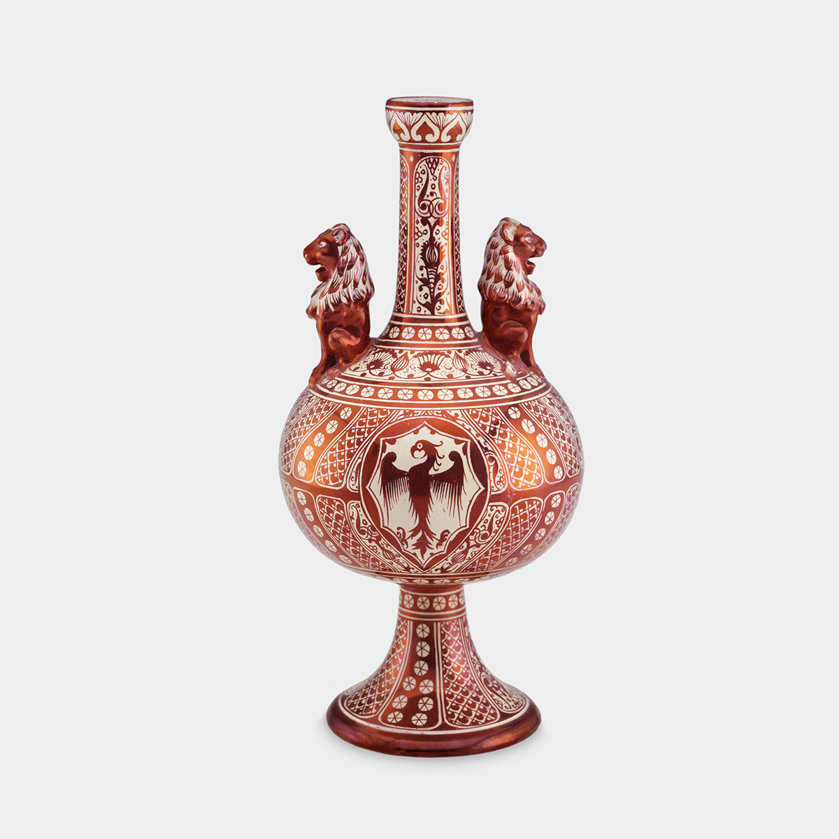 A phoenix with slightly outstretched wings and flared legs is suspended in the central emblem of this glazed ceramic vase. The vase itself has a bulbous body and narrow, elongated neck with two sculpted red lions symmetrically positioned on either side of the neck, facing outward. The vase is predominately red and white, with intricate geometric and floral patterns throughout. The neck features elongated vertical panels, each filled with a detailed vine or leaf motif, framed by solid red borders. The base continues the theme of grid-like patterns and stylized floral designs, with more white shapes against a red background, echoing the motifs from the body of the vessel. The body is adorned with alternating sections of diamond-shaped grids filled with small, white floral motifs. Between these grid sections are curved, leaf-like shapes, each filled with similar white, floral designs. The central emblem on the vase’s body depicts the phoenix within a hexagonal frame, its stylized feathers spread symmetrically along the wings and tai. The phoenix's body and heads are rendered in a solid, dark red, while its outline and detailing are in white, contrasting against the red background of the surrounding patterns. The base of the vase is flared, continuing the geometric design, with a blend of circular and diamond shapes. The ceramic of the vase has a glossy finish, giving it a reflective quality.