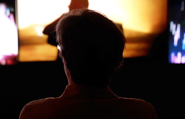 A silhouetted visitor seen from behind faces a glowing projection screen in a darkened space.