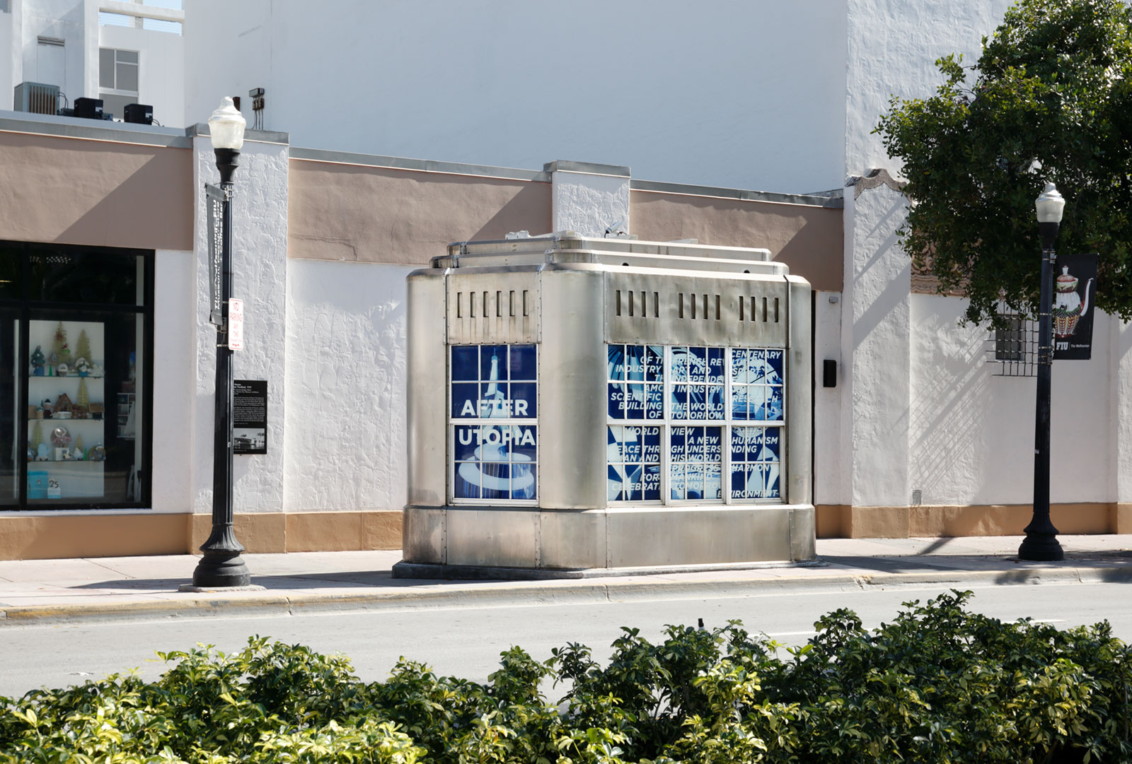 An Art Deco-style metal structure situated on a sidewalk in front of a larger building, with blue and white graphics installed in the windows