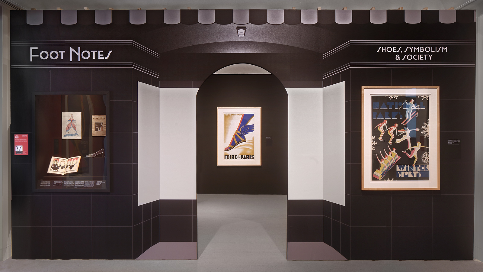 Exhibition entrance labeled “Foot Notes” and “Shoes, Symbolism & Society,” with framed posters and a central doorway