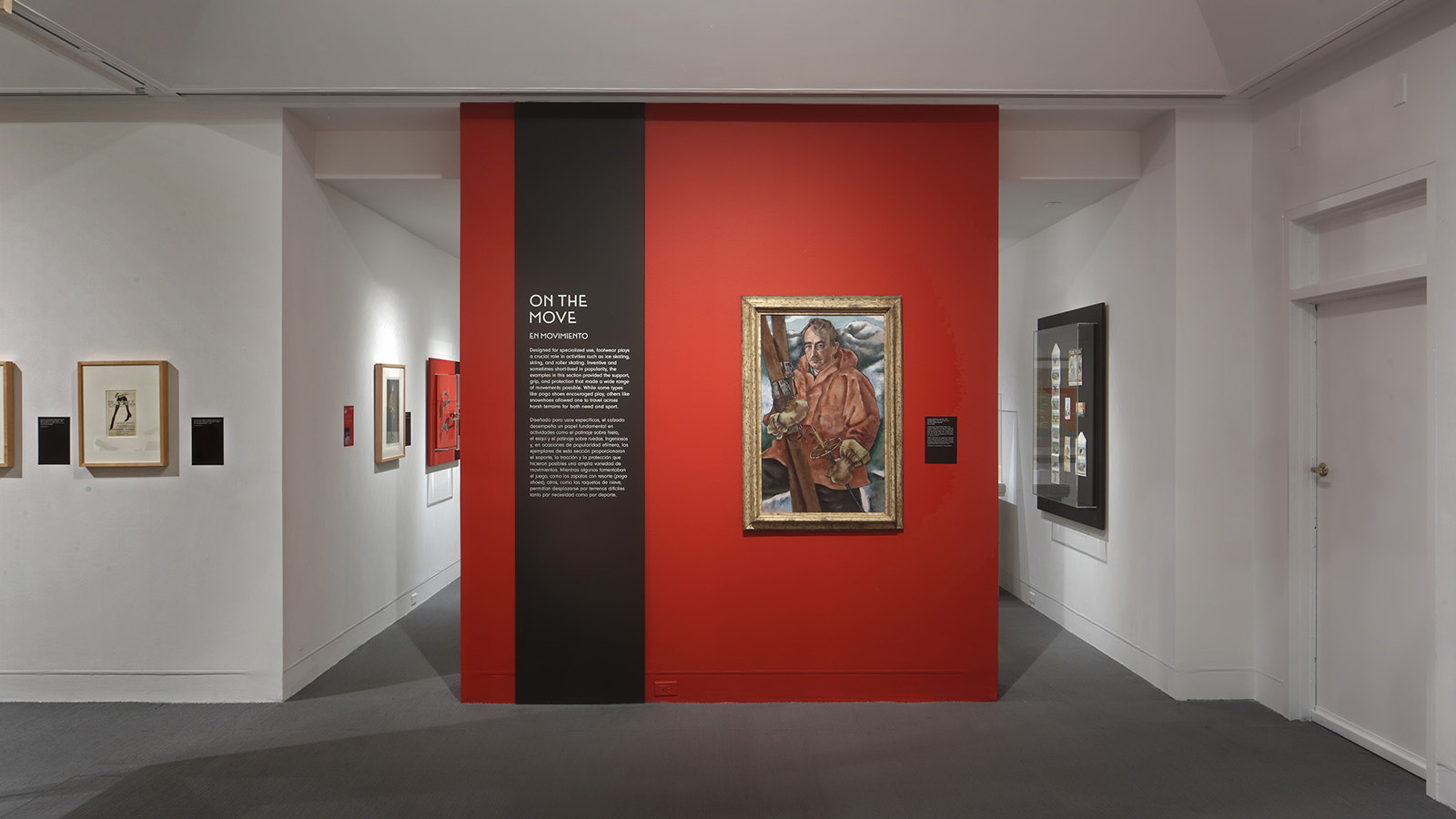 Gallery view with an “On the Move” text panel, a framed portrait on a red wall, and framed works along adjoining walls