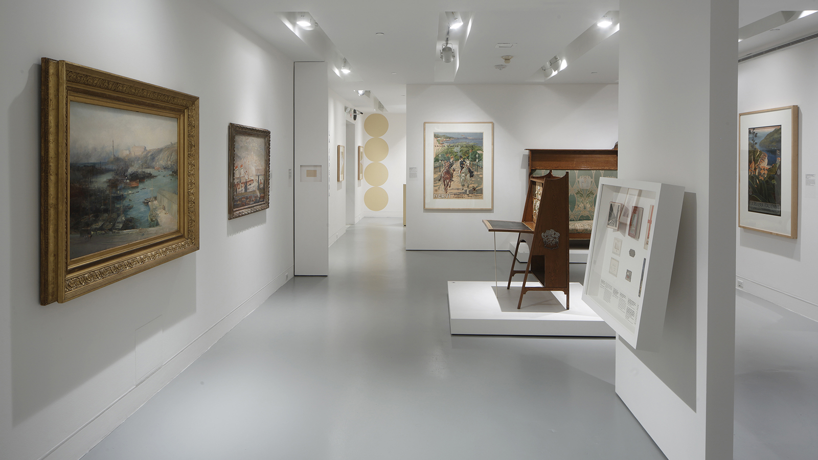 Gallery view with framed paintings and a wooden desk displayed on a white platform in the center of the room.