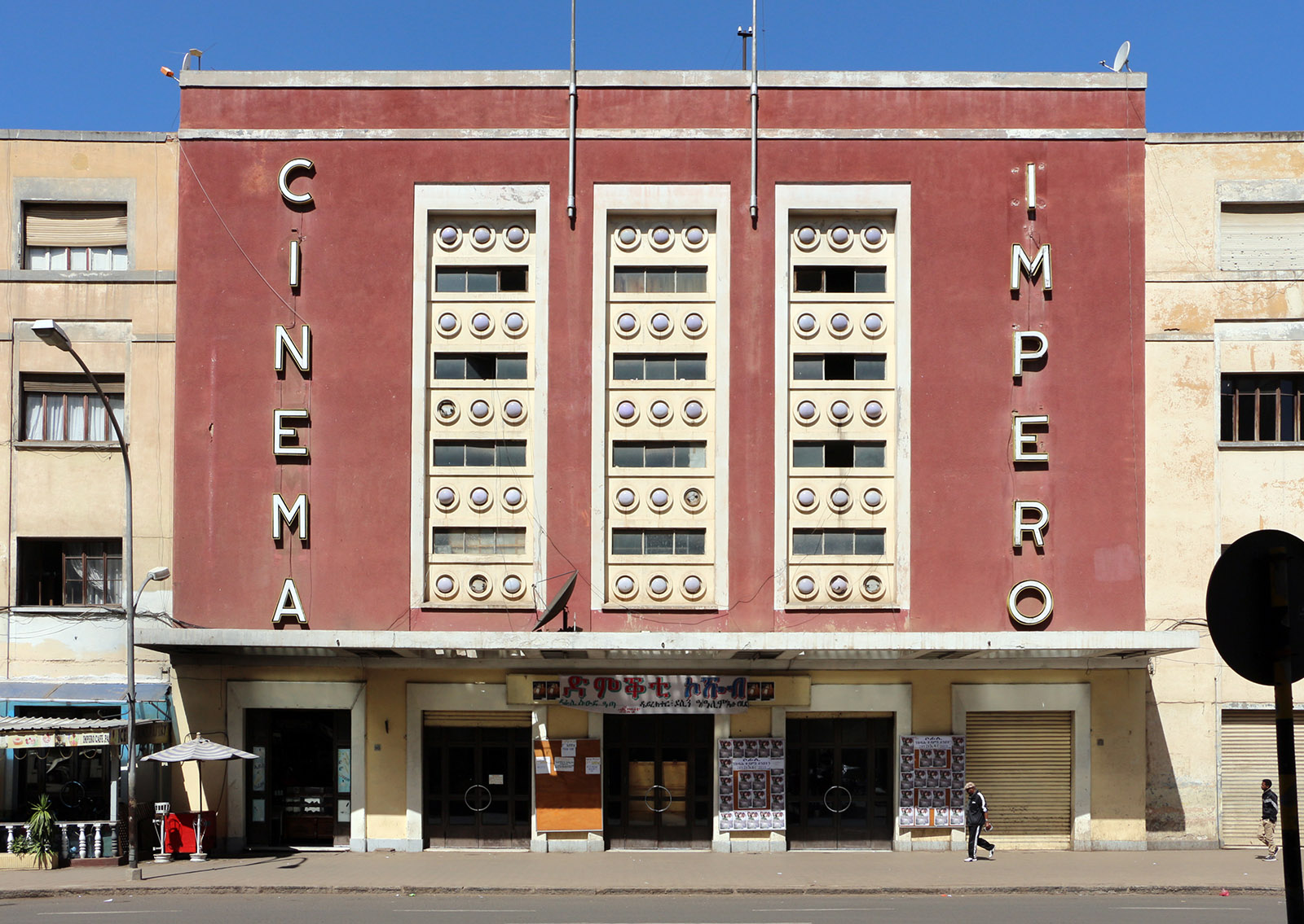 Art Deco cinema building with a red central facade, vertical 'Cinema Impero' signage, and a marquee entrance